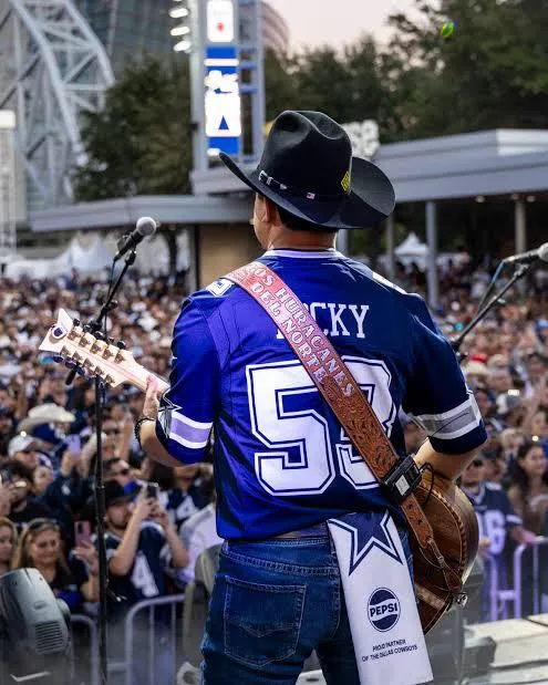 Cantor com camisa dos Cowboys tocando para o público no AT&T Stadium