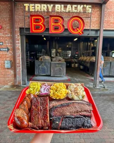Bandeja de BBQ texano com brisket, costela e linguiça na frente do Terry Black's BBQ