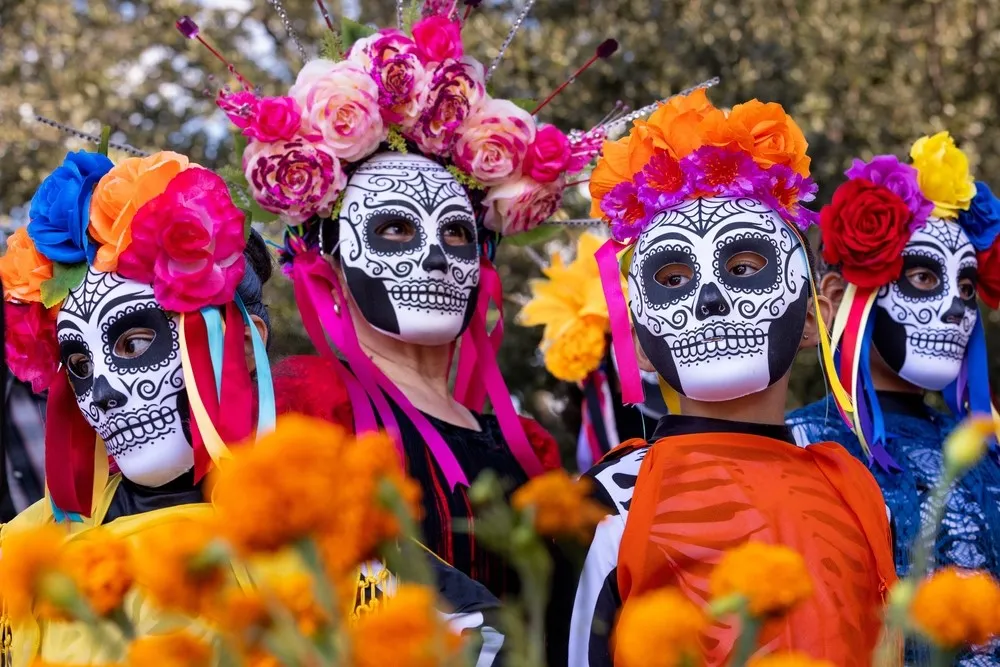 Pessoas com máscaras de caveira e coroas de flores no festival de Día de los Muertos