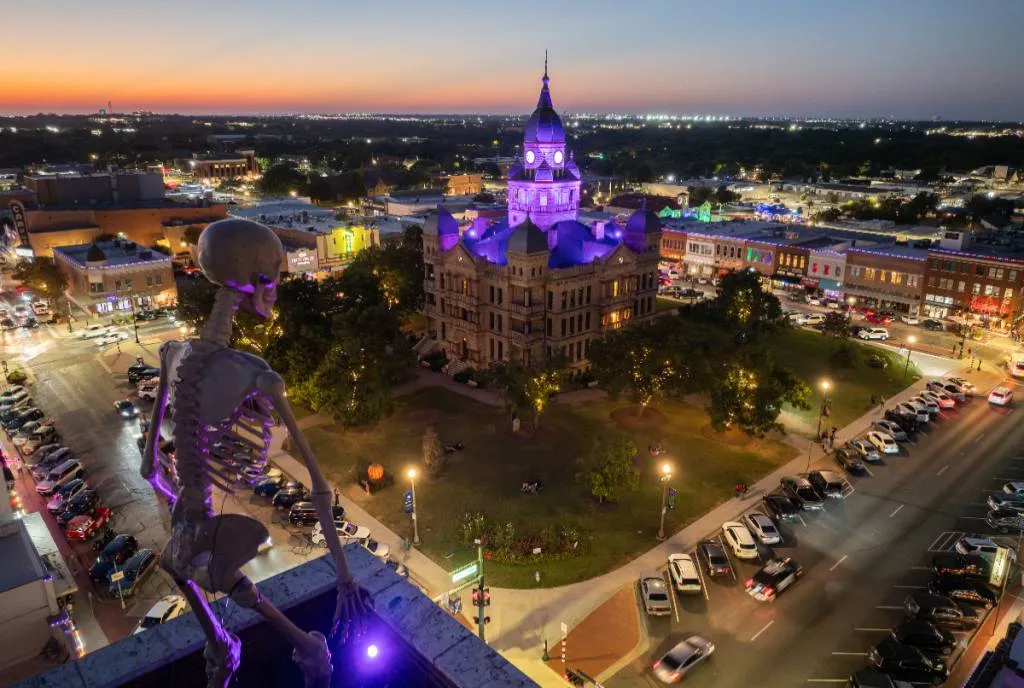 Tribunal de Denton iluminado de roxo ao anoitecer, com um esqueleto decorativo no alto de um prédio