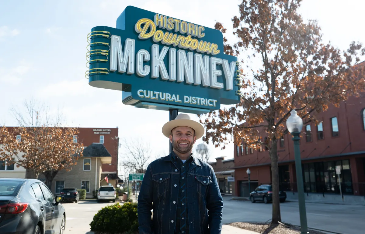 Visitante sorrindo sob o letreiro neon Historic Downtown McKinney Cultural District