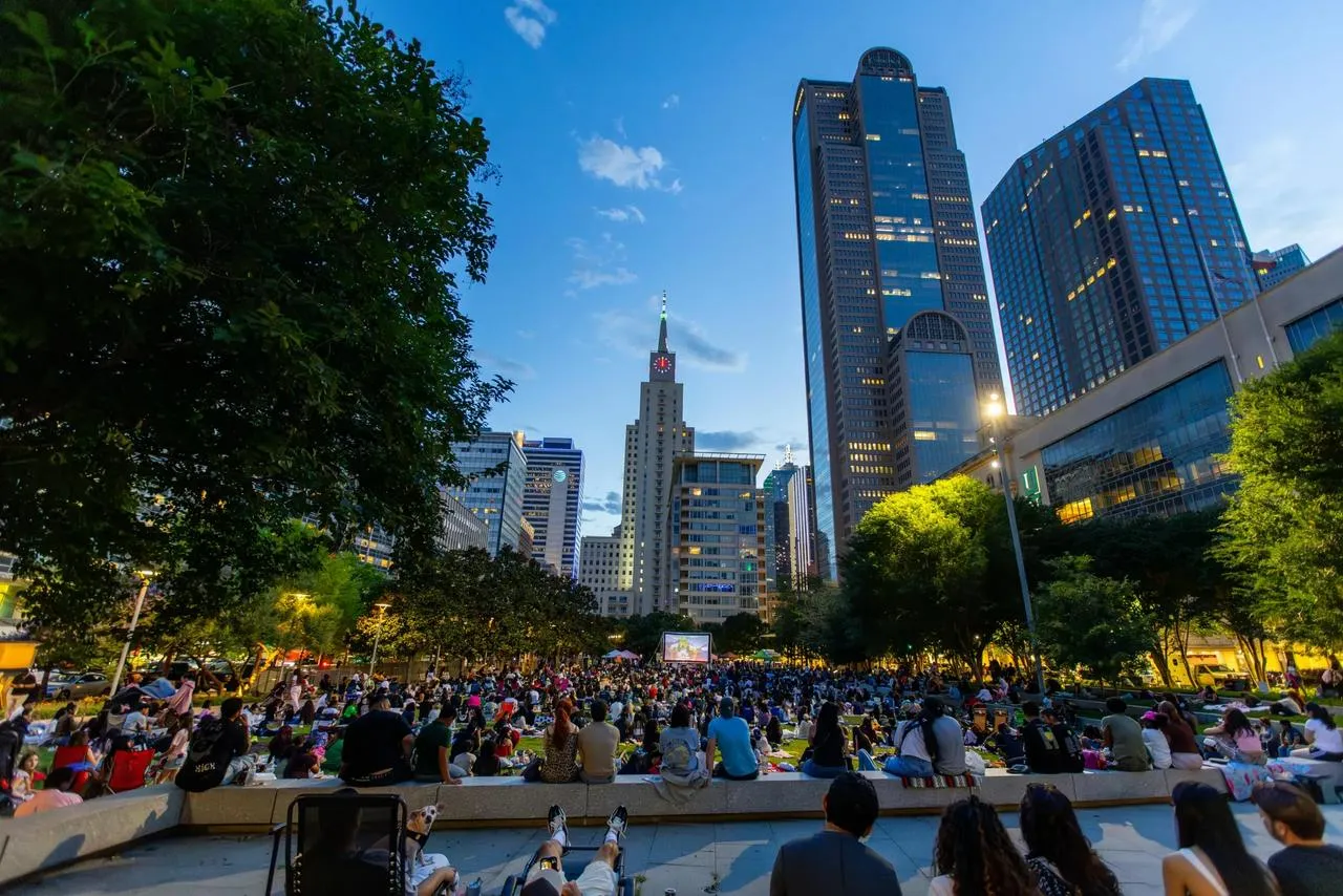 Multidão reunida no Klyde Warren Park com os arranha-céus de Dallas ao fundo