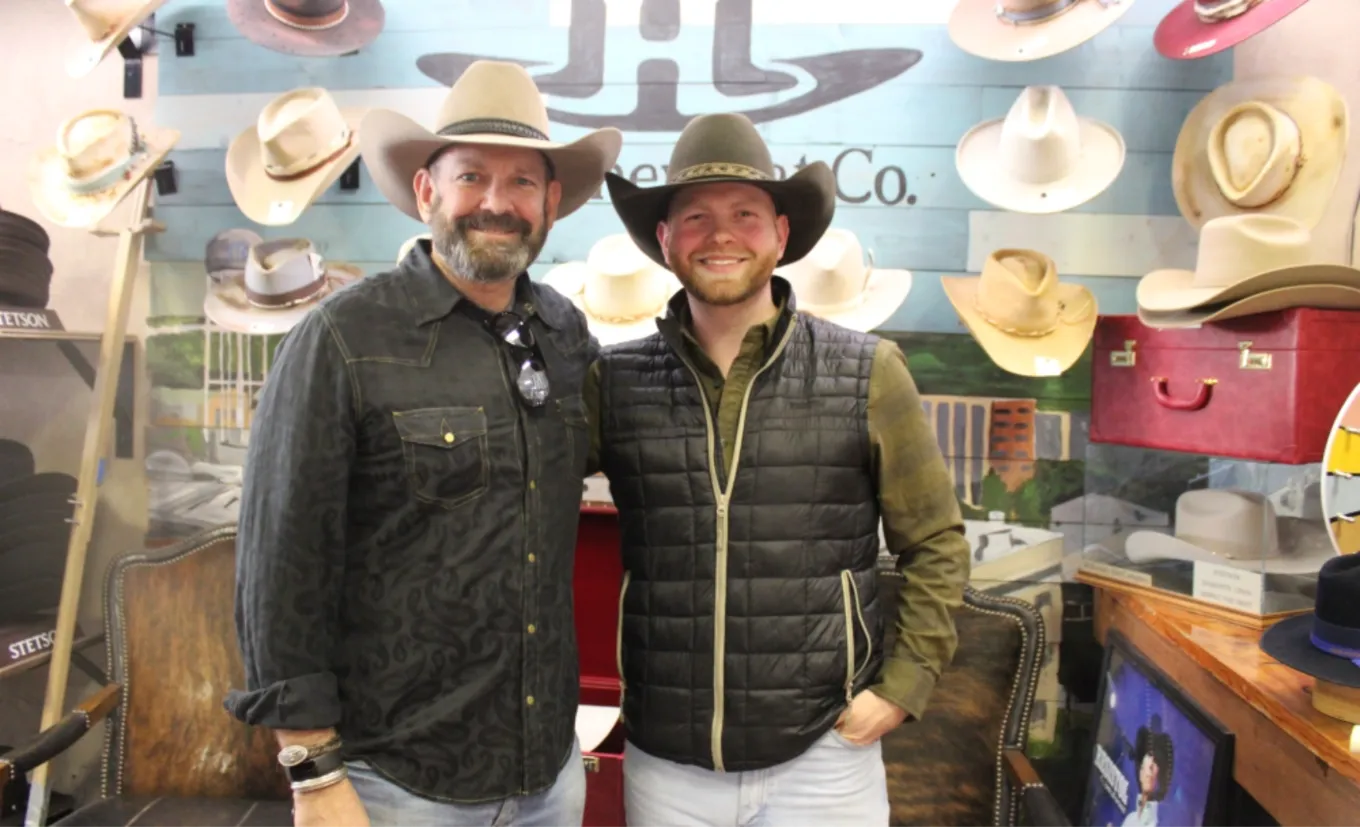 Dois homens de chapéu western na McKinney Hat Company, com chapéus Stetson na parede