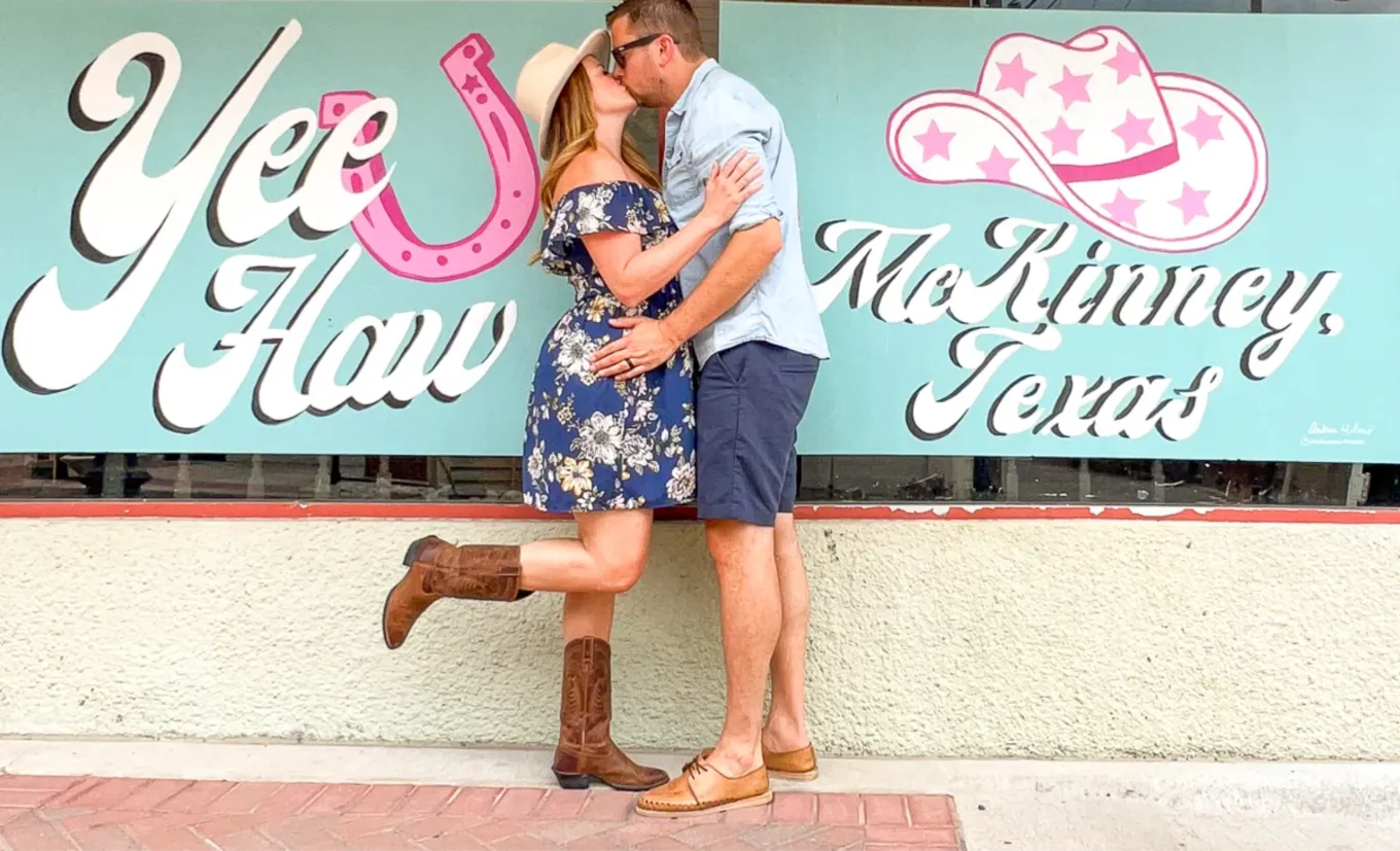 Casal se beijando em frente ao mural Yee Haw McKinney, Texas, em uma vitrine de Downtown McKinney