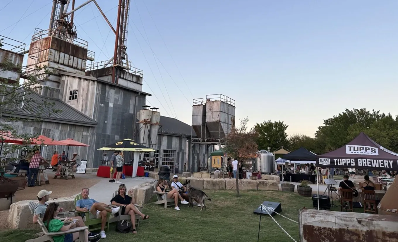 Pessoas relaxando no gramado da TUPPS Brewery, ao lado dos silos antigos, em McKinney