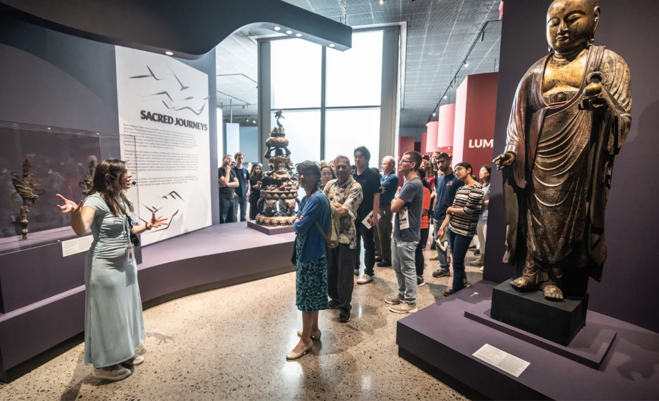 Grupo em visita guiada diante de uma estátua budista dourada no Crow Museum of Asian Art