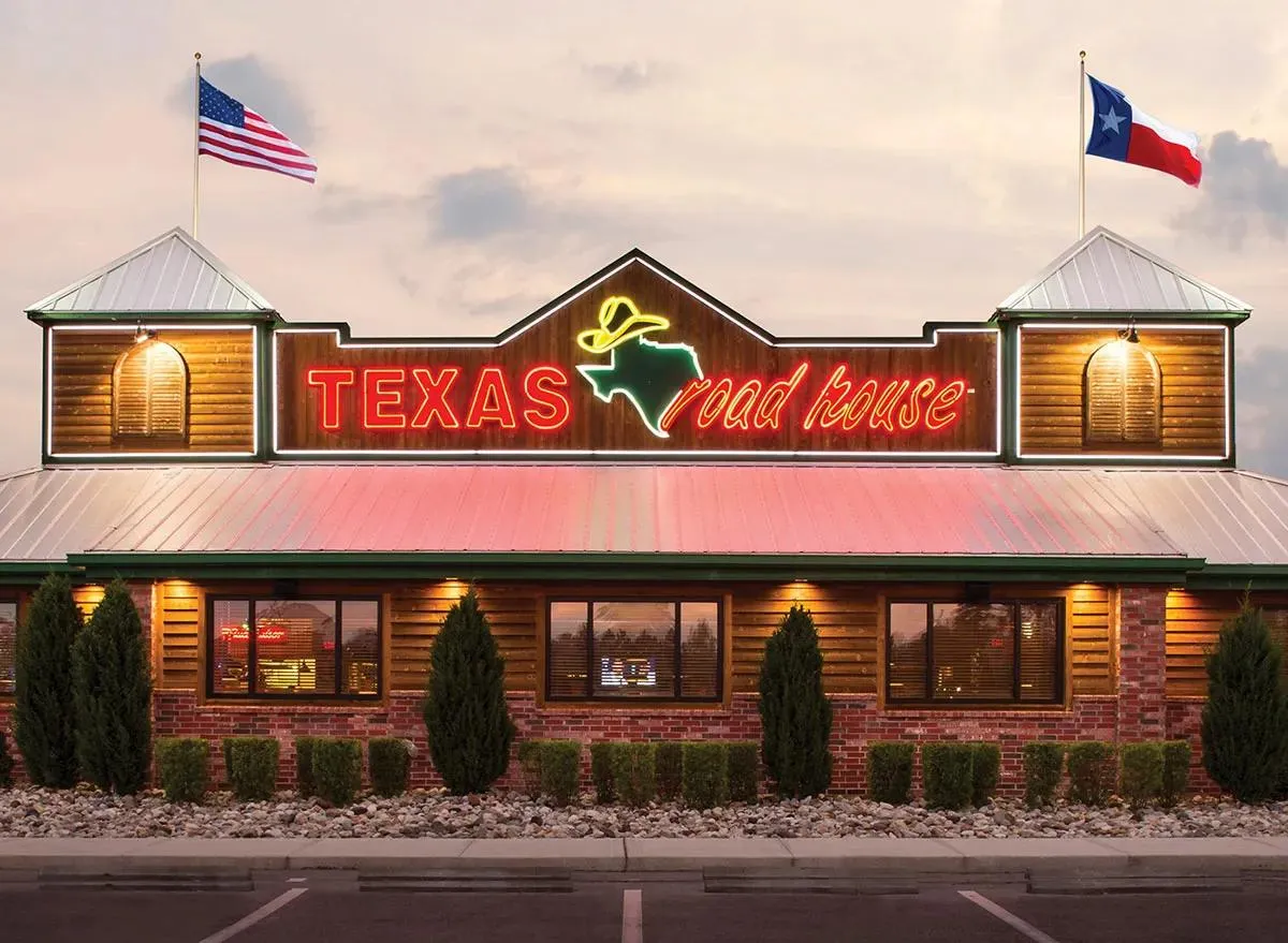 Fachada iluminada do Texas Roadhouse com as bandeiras dos EUA e do Texas