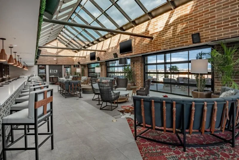 Interior do Ático em Fort Worth, com bar de mármore, teto de vidro, parede de tijolo aparente e sofás de couro