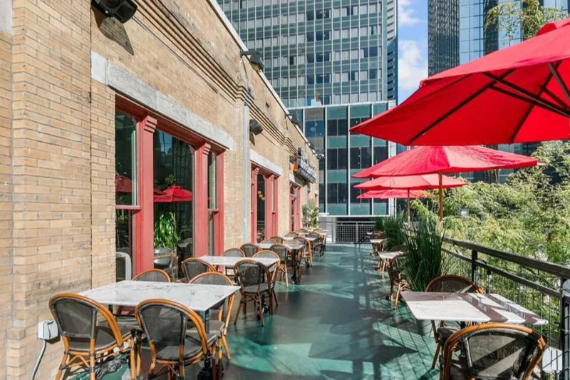 Terraço do The Woolworth em Dallas, com mesas de mármore, guarda-sóis vermelhos e prédios do Downtown ao fundo